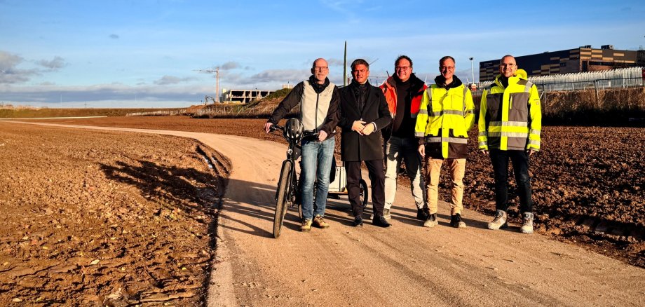 Auf einem Feldweg, dem Selztalradweg in ALzey stehen fünf Männer, einer von ihnen Bürgermeister Steffen Jung. Die beiden Männer rechts haben neon gelbe Warnwesten an. Der Mann mittig hat eine orangene Warnweste an und der Mann links außen, hält ein Fahrrad neben sich fest.