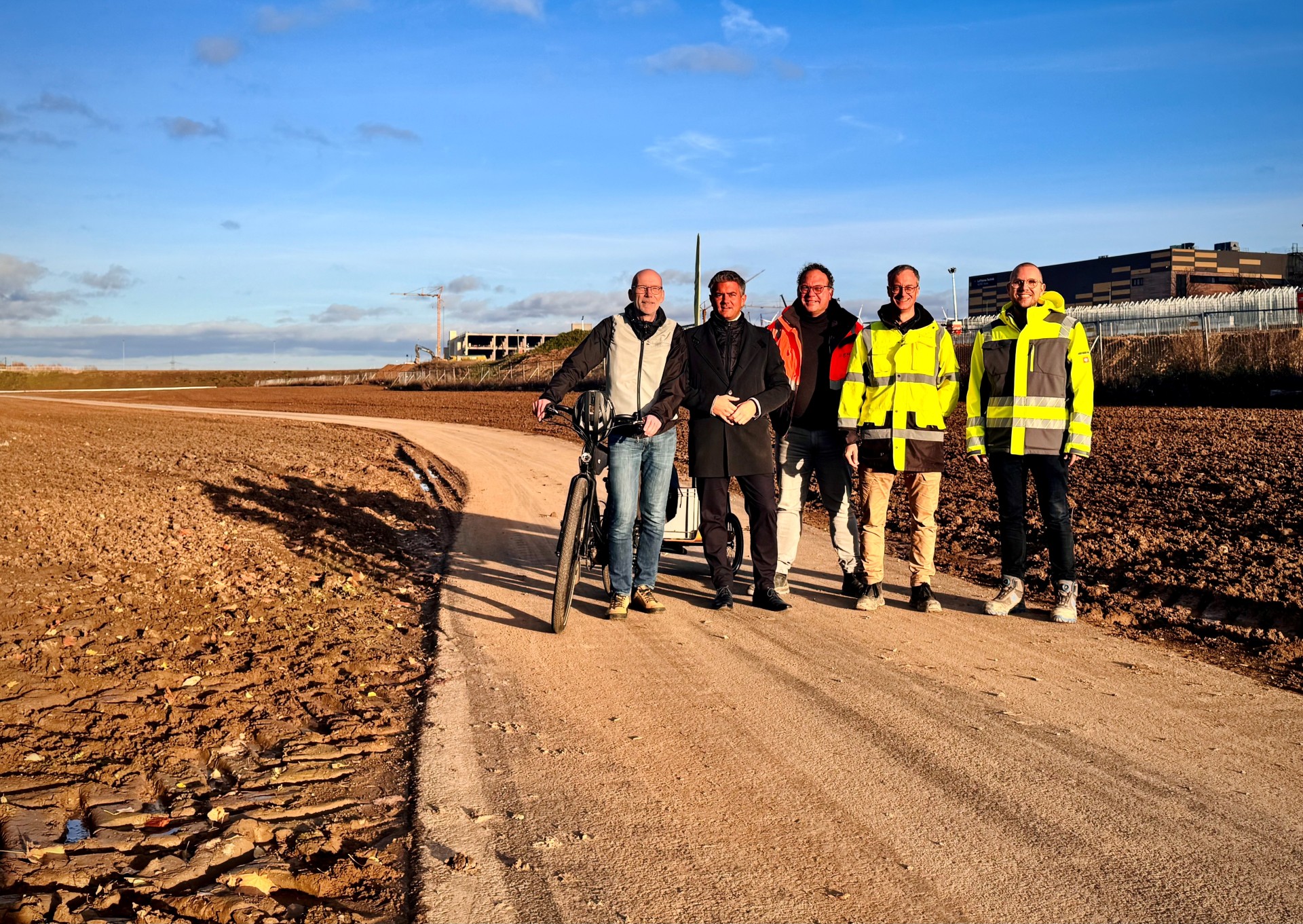 Auf einem Feldweg, dem Selztalradweg in ALzey stehen fünf Männer, einer von ihnen Bürgermeister Steffen Jung. Die beiden Männer rechts haben neon gelbe Warnwesten an. Der Mann mittig hat eine orangene Warnweste an und der Mann links außen, hält ein Fahrrad neben sich fest.