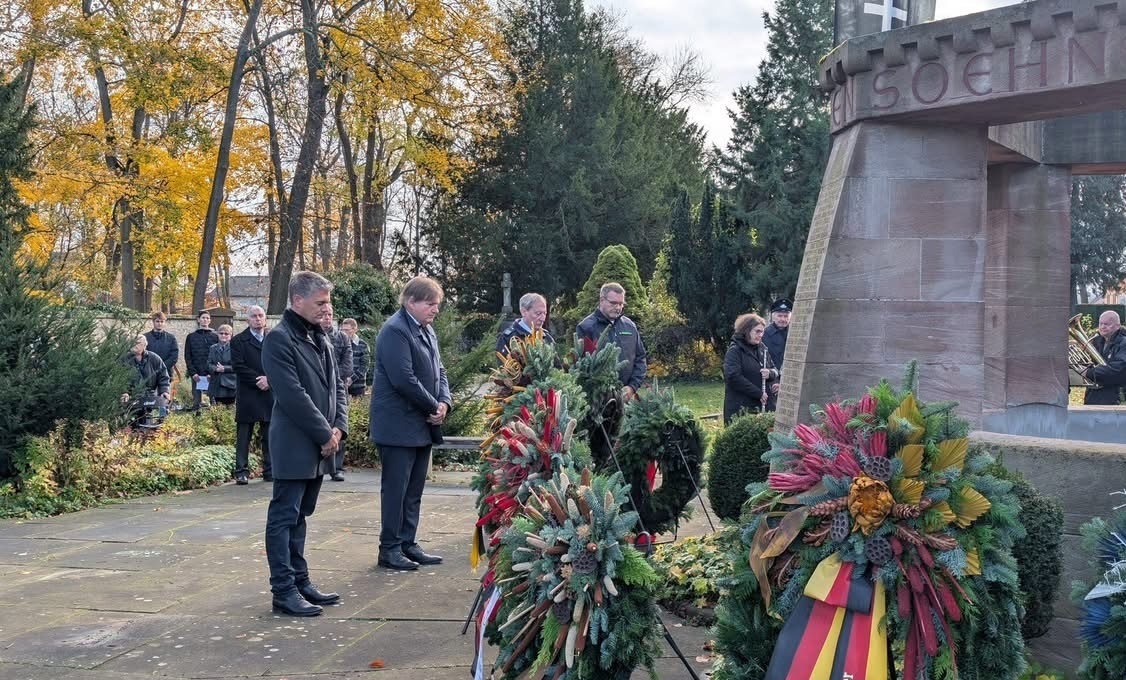 mehrere Personen, gekleidet in schwarz, stehen trauernd um eine Statue aus Stein.