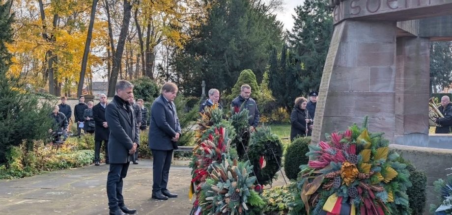 mehrere Personen, gekleidet in schwarz, stehen trauernd um eine Statue aus Stein.