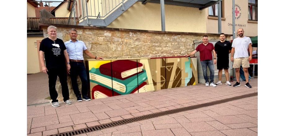 Stromkästen die bunt angemalt wurden in der Stadt Alzey und fünf Männer daneben, einer davon Bürgermeister Steffen Jung