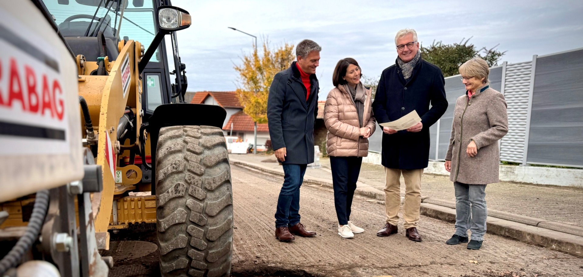 Ministerin Schmitt und Bürgermeister Steffen Jung stehen an der Ortsdurchfahrt Dautenheim und schauen sich gemeinsam einen Plan neben einem gelben Bagger an.