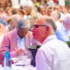 Hier sieht man eine Nahaufnahme von Besuchern der Weinprobe am Winzerfest, wie sie am Tisch sitzen und Wein trinken.
