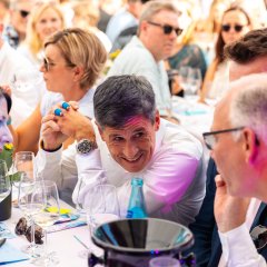 Auf dem Bild sieht man eine Nahaufnahme von Dr. Markus Merk, wie er sich an der Weinprobe mit seinen Tischnachbarn unterhält.