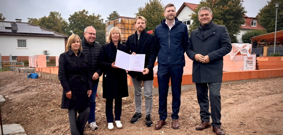 Einige Personen, darunter Bürgermeister Steffen Jung, stehen auf einer Baustelle in Schafhausen. Eine Person hält den Förderbescheid für ein neues klimagerechtes Wohnprojekt hoch.