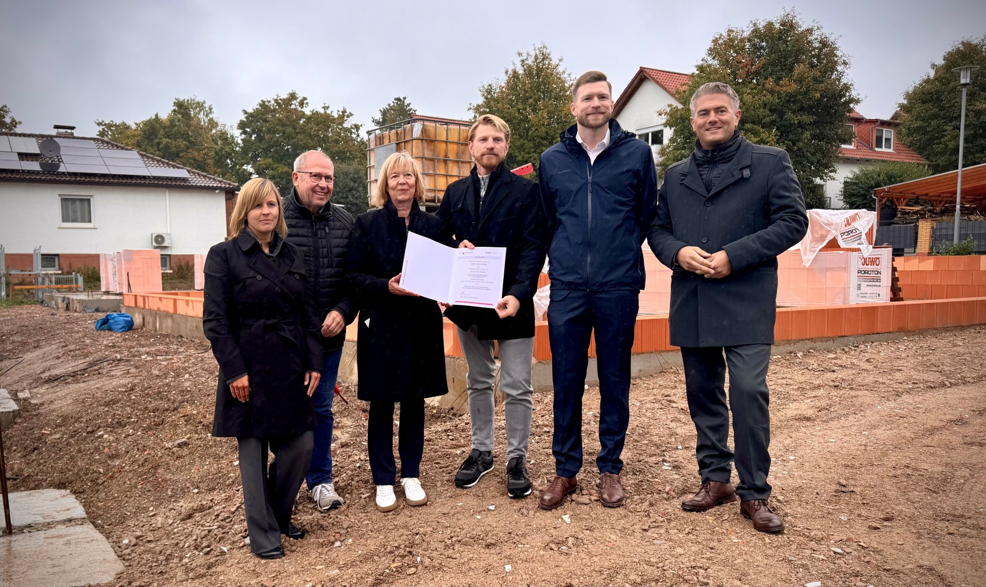 Einige Personen, darunter Bürgermeister Steffen Jung, stehen auf einer Baustelle in Schafhausen. Eine Person hält den Förderbescheid für ein neues klimagerechtes Wohnprojekt hoch.