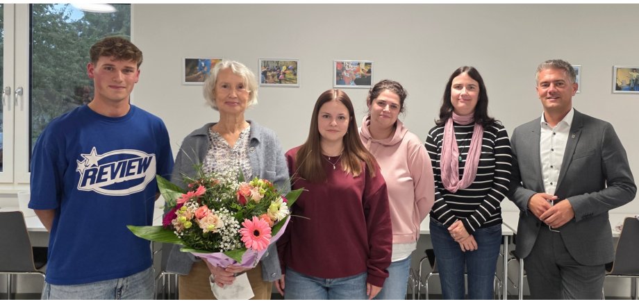 Städtische Kitas und Schulen feiern eigene Feierstunde: Willkommen und Abschied in einem starken Team Auf dem Bild sieht man 6 Personen. Ganz außen rechts steht Bürgermeister Steffen Jung. Eine Frau hat einen bunten Blumenstrauß in der Hand.