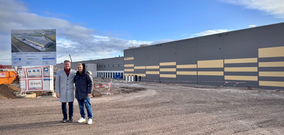 Man sieht die Baustelle des neuen TST-Logistikzentrum von außen und Bürgermeister Steffen Jung der in die Kamera lächelt.