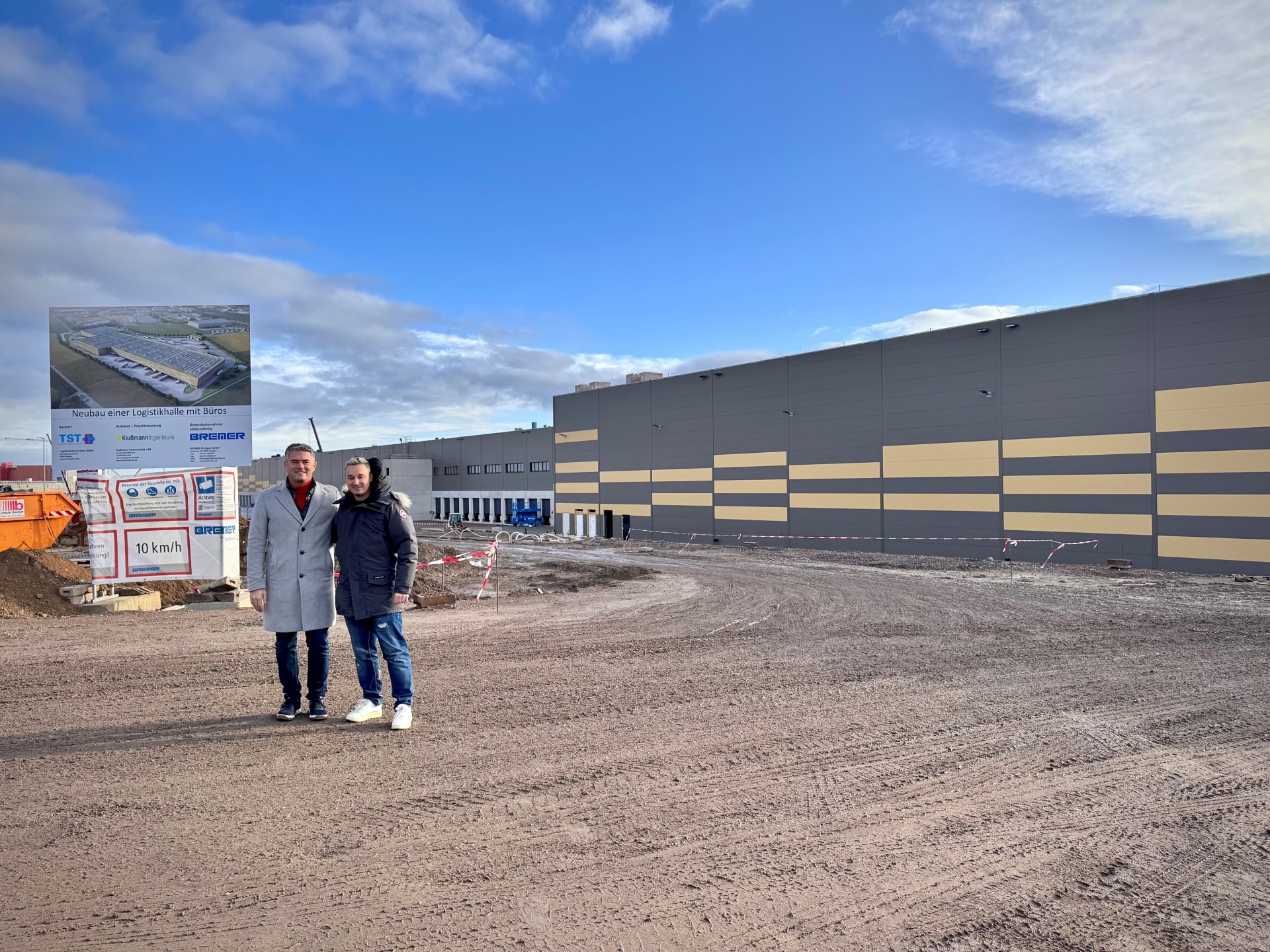 Man sieht die Baustelle des neuen TST-Logistikzentrum von außen und Bürgermeister Steffen Jung der in die Kamera lächelt.