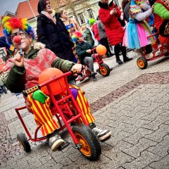 Kinderfastnachtsumzug als Clown verkleidete Kinder die eine Straße entlanag laufen und fahren auf Dreirädern