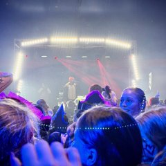 Man sieht eine Bühne im Hintergrund und einige Köpfe im vordergrund des Bildes