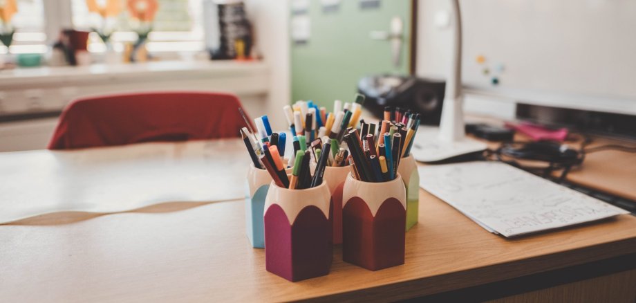 Man sieht einen Schreibtisch, mehrere Stiftbehälter und Stifte sowie Schreibmaterial.