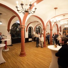 Ein heller Raum in der Stadthalle mit einigen Stehtischen an denen Menschen stehen und Bürgermeister Steffen Jung am Rednerpult.