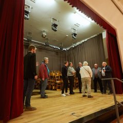 Ein Bild von der Bühne der Stadthalle auf der einige Menschen stehen und sich unterhalten.