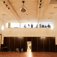 Ein Bild der Stadthalle auf denen man einige Menschen sieht die sich unterhalten oder Bilder machen.