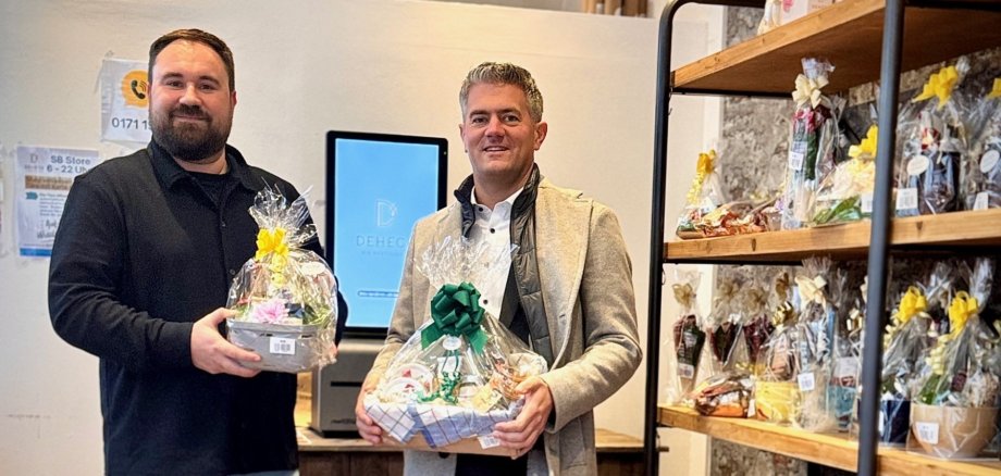 Florian Stenner und Bürgermeister Steffen Jung im Selbstbedienungsladen Deheck mit Geschenkkörben und Geschenksets neben einem Regal mit Geschenkkörben und Geschenksets.