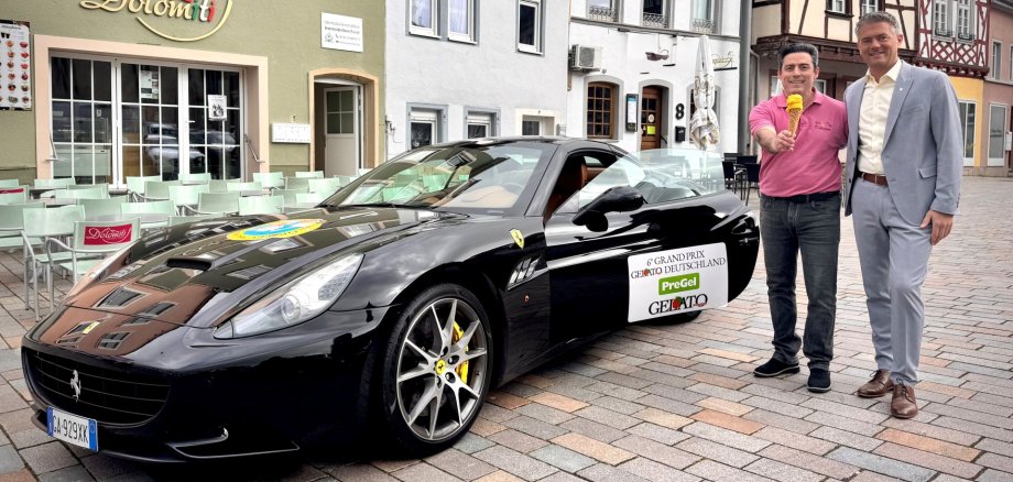 Bürgermeister Steffen Jung und Giuseppe der Besitzer des Eisladens mit seinem Mango-Eis und auch seinem gewonnenen Ferrari auf dem Grand Prix Gelato Deutschland steht.