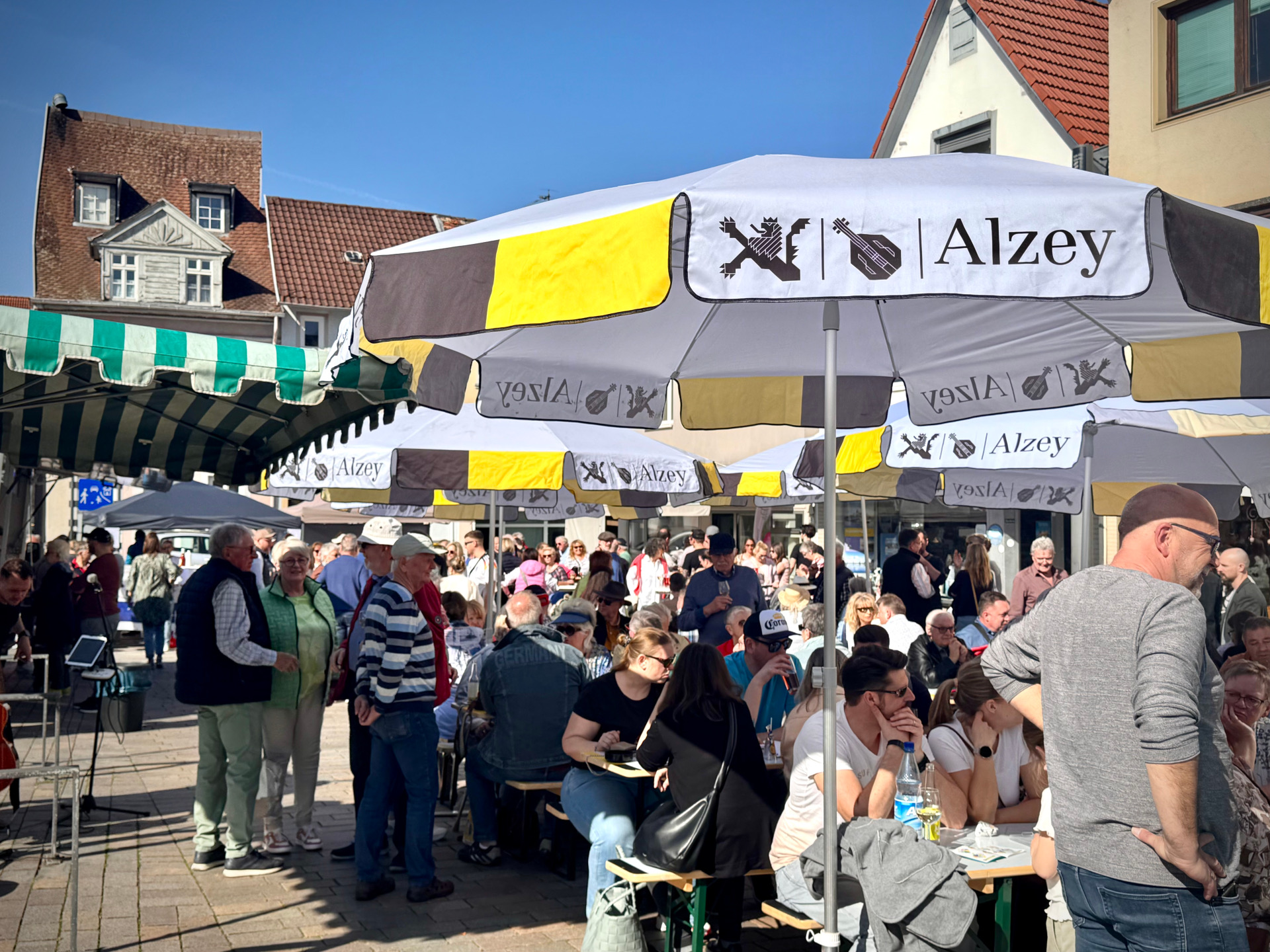 Man sieht den Wochenmarkt, Menschen die sitzen, stehen, trinken und sich unterhalten.