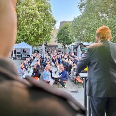 ein Mann steht auf der Bühne und hält eine Rede vor Publikum, die Kamera steht hinter ihm und fotografiert an ihm vorbei in die Menschenmenge rein