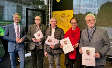 Auf einer Bühne stehen fünf Personen und lachen in die Kamera. Eine von ihnen ist Bürgermeister Steffen Jung (links). Daneben stehen drei Männer und eine Frau mit jeweils einer Urkunde in der Hand.