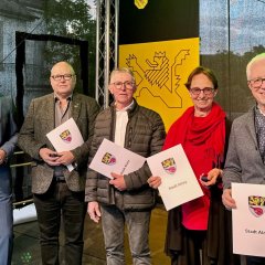 Auf einer Bühne stehen fünf Personen und lachen in die Kamera. Eine von ihnen ist Bürgermeister Steffen Jung (links). Daneben stehen drei Männer und eine Frau mit jeweils einer Urkunde in der Hand.