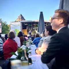 Einige Menschen sitzen an einem Tisch in Richtung einer Bühne. Es wurde durch sie durch fotografiert richtung Bühne.