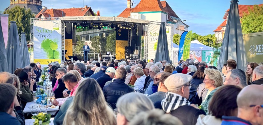 eine Menschenmasse steht vor einer Bühne mit der Aufschrift Scheu time, die Köpfe sind alle in Richtung Bühne gerichtet