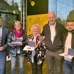 Auf einer Bühne stehen fünf Personen und lachen in die Kamera. Eine von ihnen ist Bürgermeister Steffen Jung (links). Daneben stehen zwei Männer und zwei Frauen mit jeweils einer Urkunde in der Hand.