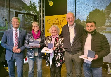 Auf einer Bühne stehen fünf Personen und lachen in die Kamera. Eine von ihnen ist Bürgermeister Steffen Jung (links). Daneben stehen zwei Männer und zwei Frauen mit jeweils einer Urkunde in der Hand.