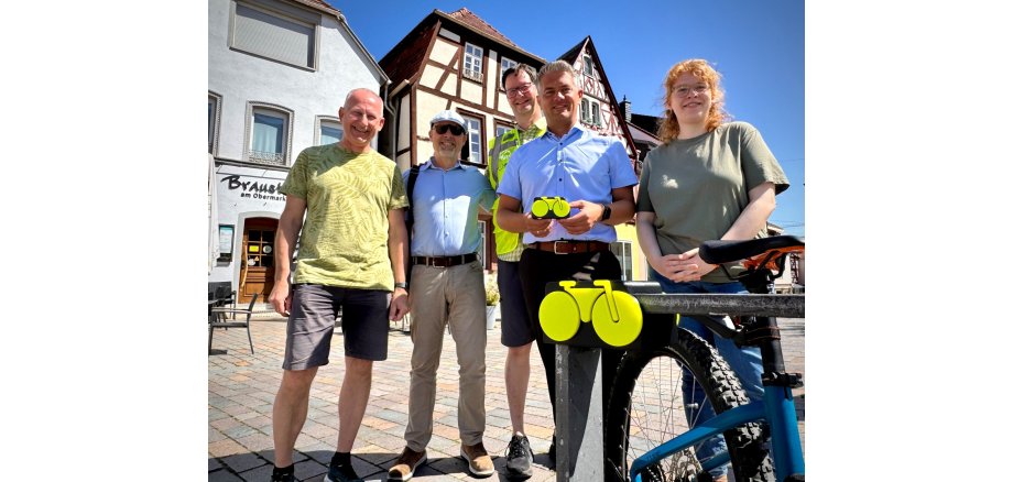 fünf Personen stehen vor der Kamera und lachen in diese, mittig steht Bürgermeister Steffen Jung und hält ein kleines gelbes Modellfahrrad in die Kamera