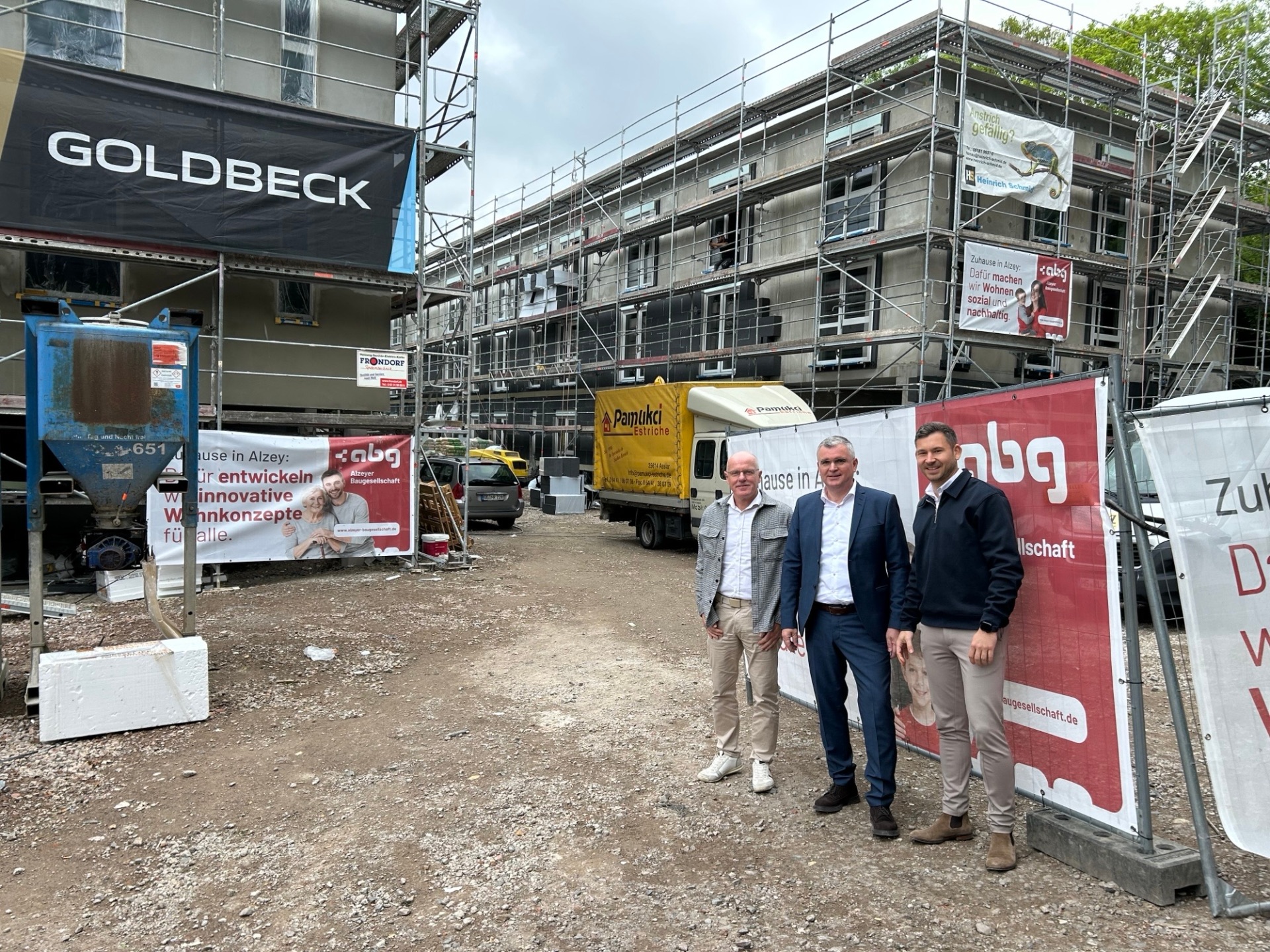 drei Männer in Anzug stehen vor einer Baustelle