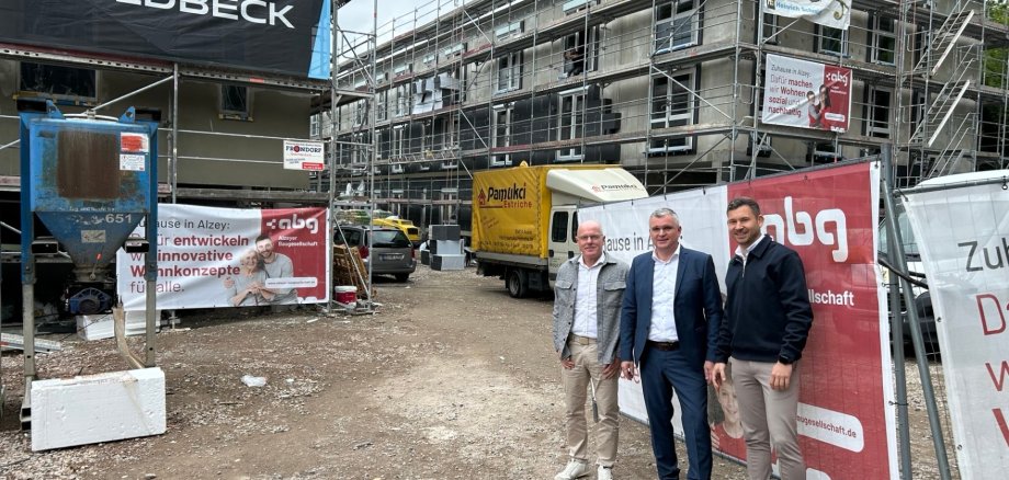 drei Männer in Anzug stehen vor einer Baustelle