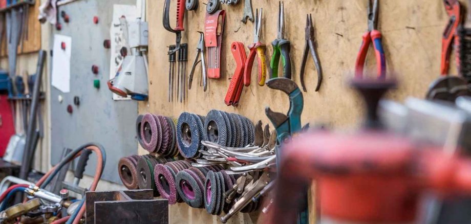 Man sieht eine Holzwand einer Werkstatt, an der viele verschiedene Werkzeuge hängen.