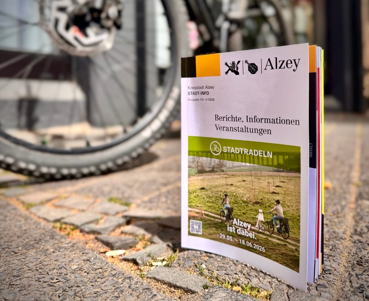 die neuste Ausgabe der Stadtinfo mit der Stadtradelaktion auf dem Titelbild steht auf dem Boden vor einem Fahrrad