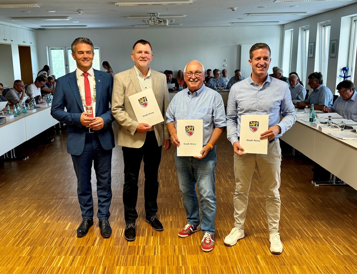 Die Stadtspitze ist komplett: Bürgermeister Steffen Jugn beglückwünscht die neuen Beigeordneten Klaus Kübler, Dr. Hans-Werner Stark und Michael Lohmer. Vier Personen stehen mit Urkunden in der Hand in einem Sitzungssaal voller Menschen.