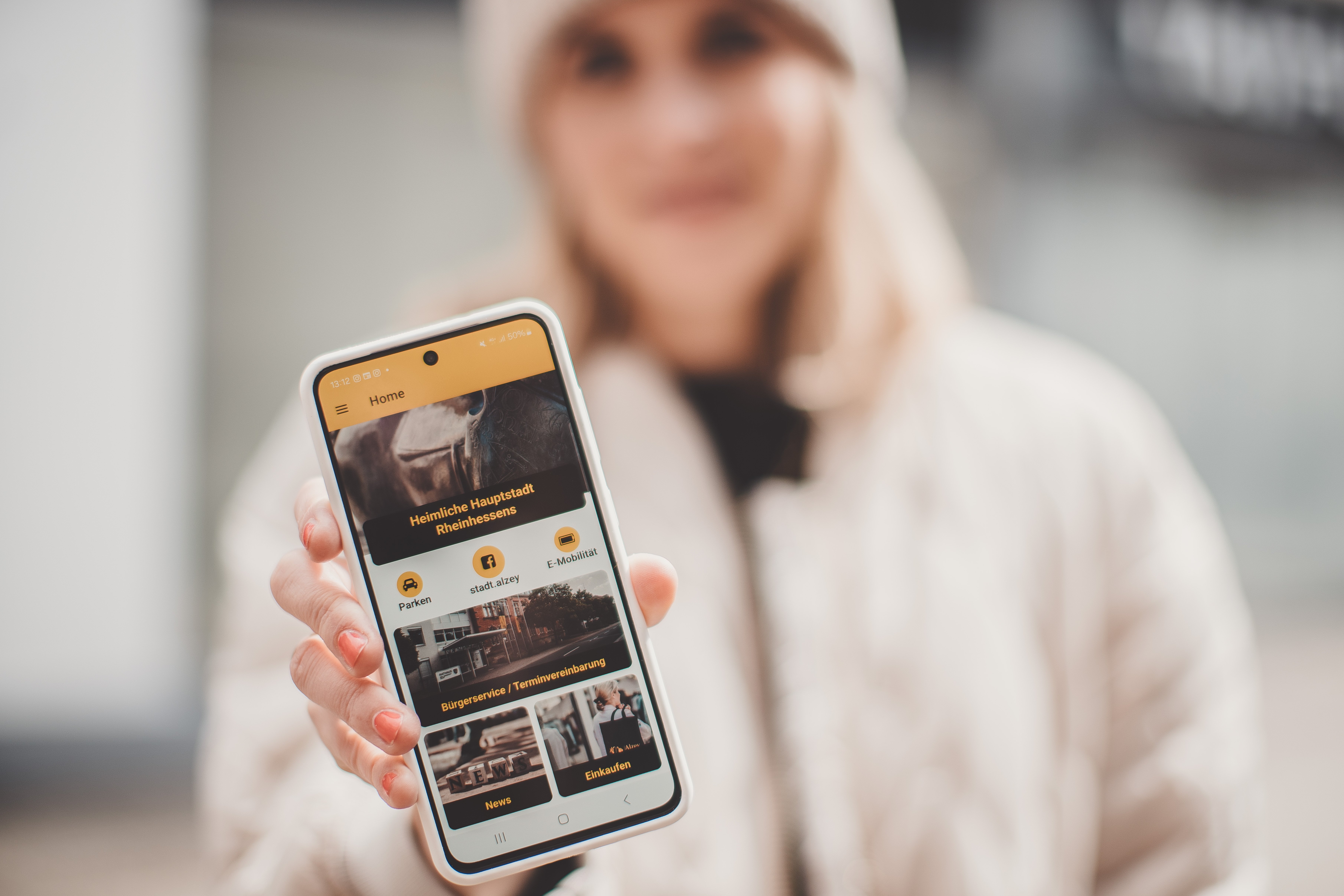 Die Stadt-App Eine Frau hält ein Smartphone in die Kamera, auf dem die Stadt-App zu sehen ist.