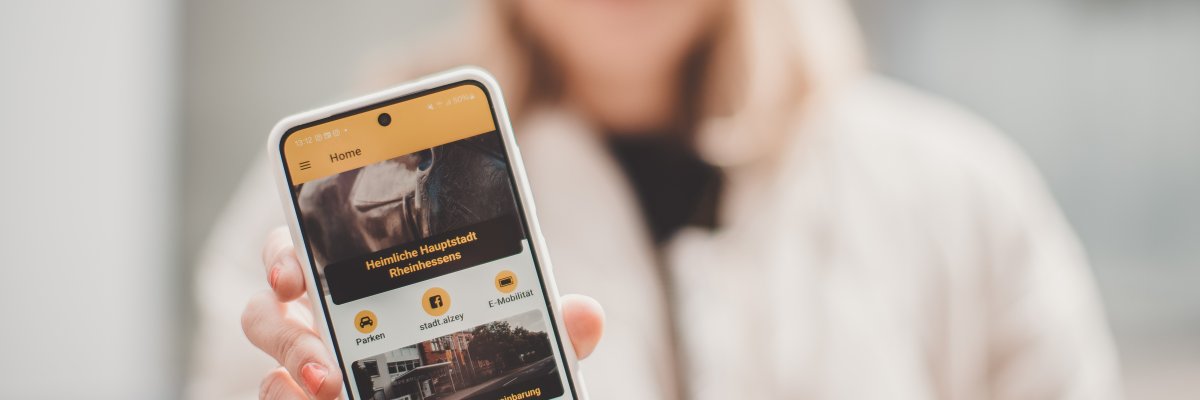 Eine Frau hält ein Smartphone in die Kamera, auf dem die Stadt-App zu sehen ist.