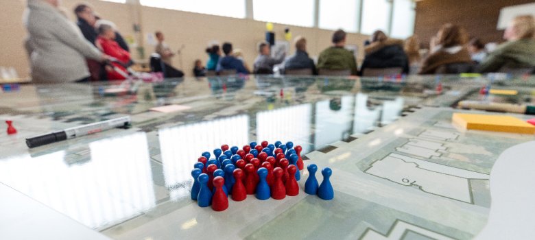 blaue und rote Figuren auf einem Stadtplan hinter einer Menschenversammlung