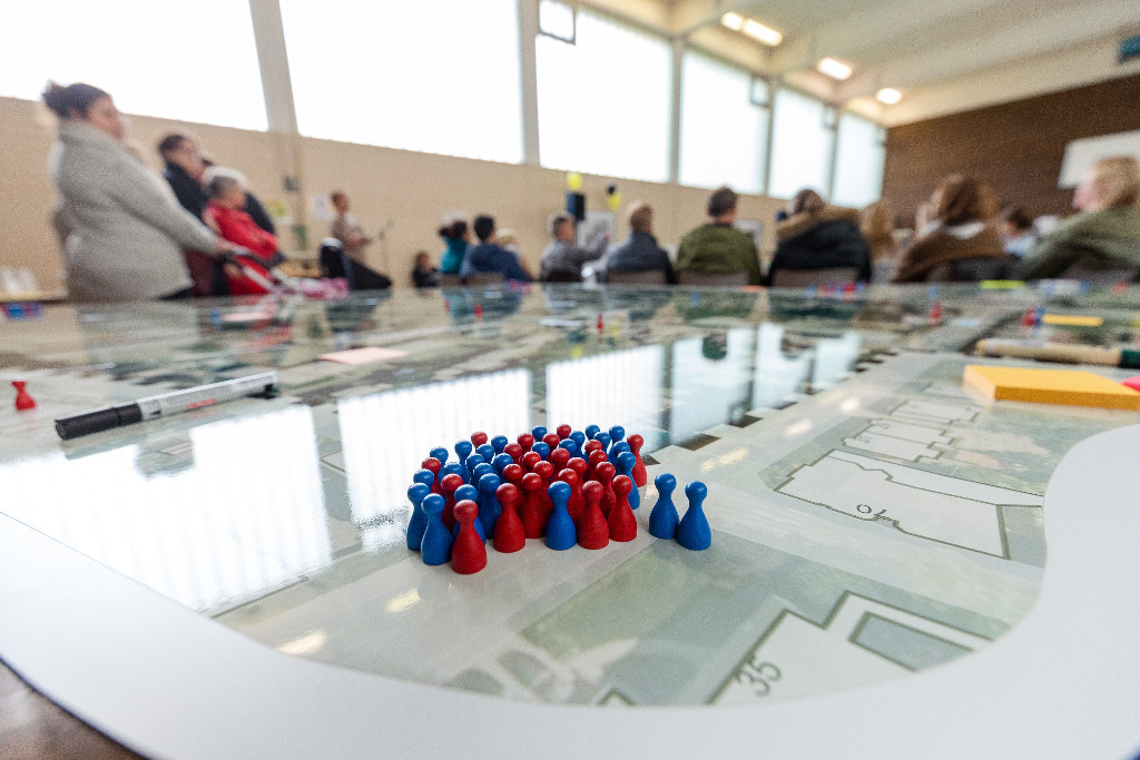 blaue und rote Figuren auf einem Stadtplan hinter einer Menschenversammlung